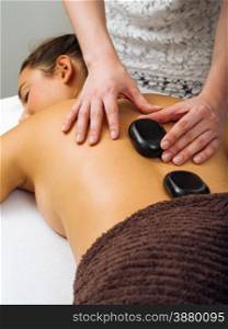 Photo of a young woman lying in a spa having a hot stone treatment. Focus on the hands of the masseuse.