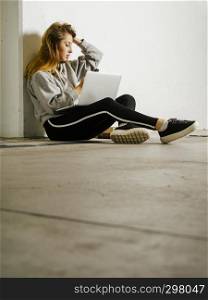Photo of a young woman student sitting in a hallway with a laptop, cell phone, and books.