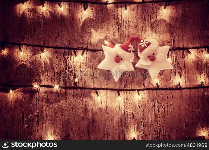 Photo of abstract Christmas glowing background, yellow electrical garland on old wooden door, shiny decorations on dark grunge wall, two Santa Claus stars, New Year festive ornament