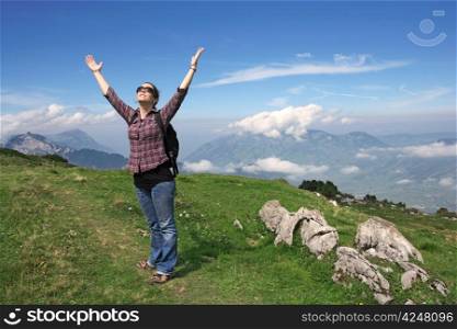 Photo of an active female with backpack and hands pointing to the sky while hiking up a mountain trail.