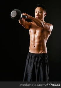 Photo of an Asian male exercising with a kettle bell over dark background.