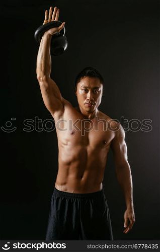 Photo of an Asian male exercising with a kettle bell over dark background.