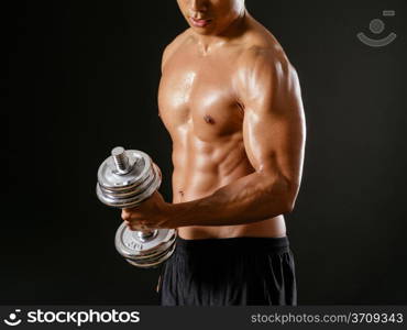Photo of an Asian male exercising with dumbbells and doing bicep curls over dark background.