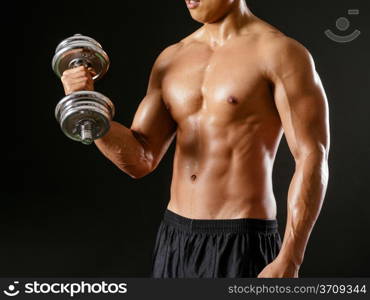 Photo of an Asian male exercising with dumbbells and doing bicep curls over dark background.