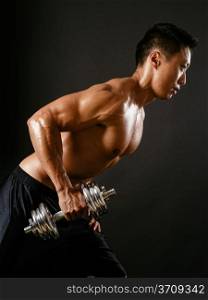 Photo of an Asian male exercising with dumbbells and working his triceps over dark background. Focus is on the arm.