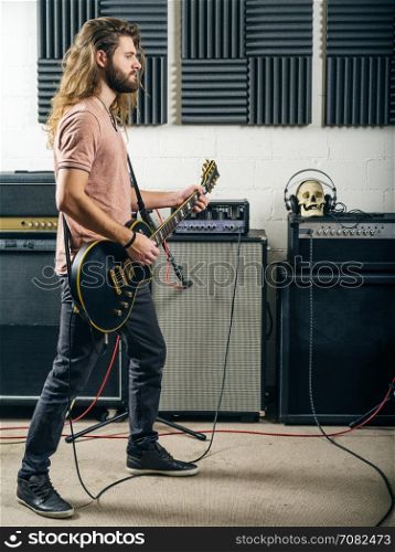 Photo of an attractive man playing electric guitar in a recording studio.
