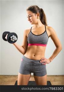Photo of an attractive woman doing a dumbbell curl while standing.