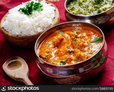 Photo of an Indian meal of Butter Chicken, rice and Saag Paneer. Focus across the Butter Chicken bowl.
