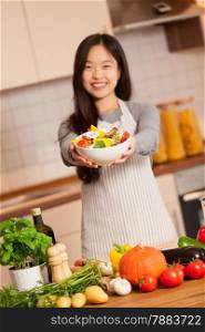 photo of asian smiling woman holding a colorful salad in her hands in the kitchen