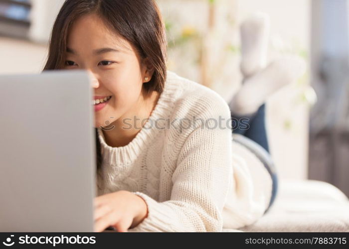 photo of asian smiling woman working with her computer at home on the sofa