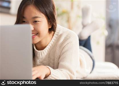 photo of asian smiling woman working with her computer at home on the sofa