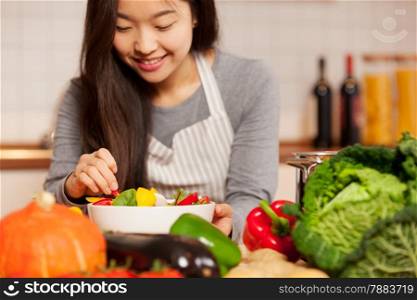 photo of asian young woman composing a colorful salad at home in the kitchen
