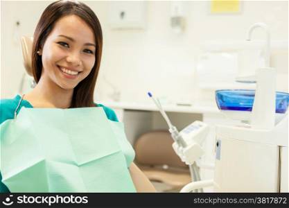 photo of asian young woman sitting at the dentist while smiling towards the camera