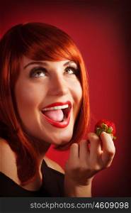 Photo of attractive red head woman eat sweet strawberry, closeup portrait of playful girl with open mouth and looking up isolated on red background, healthy lifestyle, pleasure and seduction concept