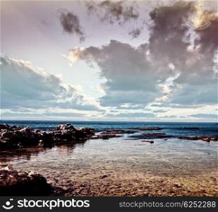 Photo of beautiful stony coast, rocky beach, dramatic sunset, cloudy sky, stunning seascape, summertime vacation, travel and tourism concept
