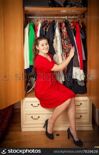 Photo of beautiful woman in red dress sitting at big wardrobe