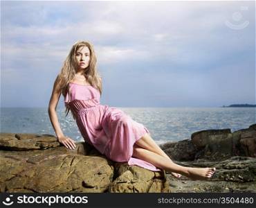 Photo of beautiful woman in wet clothes on a rocky seashore