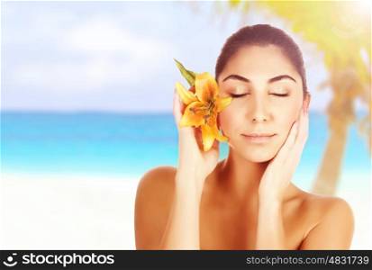 Photo of beautiful woman on the beach with yellow lily flower in head, arabic female with closed eyes enjoying dayspa, beauty treatment, body care, luxury tropical resort, vacation and travel concept&#xA;