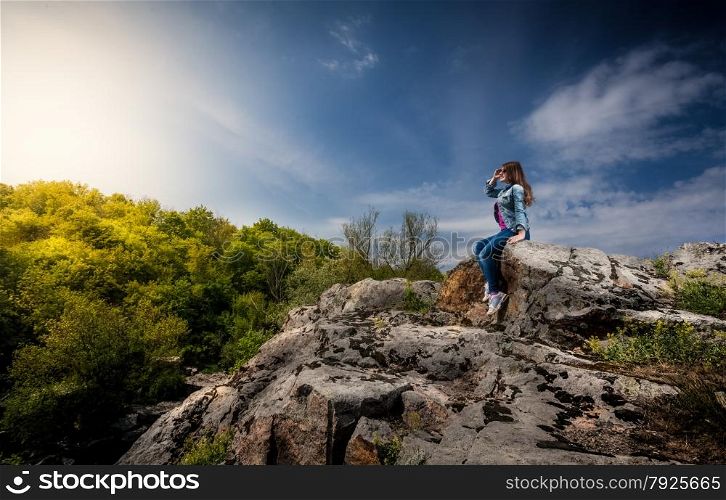 Photo of beautiful woman sitting on top of cliff and looking at sunset