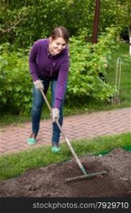 Photo of beautiful woman working with rake on garden bed