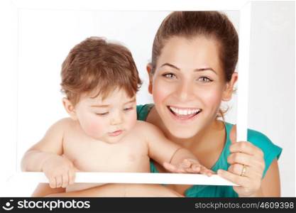 Photo of beautiful young mother with cute baby boy holding white frame, pretty woman carrying little son isolated on white background, smiling faces, healthy lifestyle, happy motherhood concept