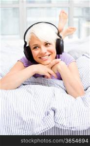 Photo of blonde woman listening to mus&#xA;ic with headphones in the bed