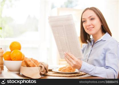 Photo of brunette businesswoman reading the newspaper while having breakfast at home