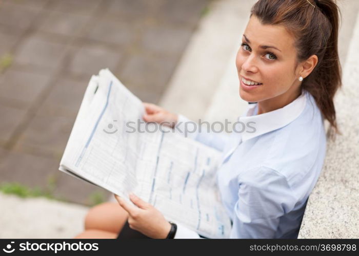 photo of brunette businesswoman sitting on stairs with newspaper