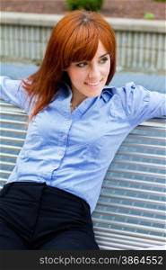 Photo of businesswoman with red hair sitting outside on a metal bench while smiling