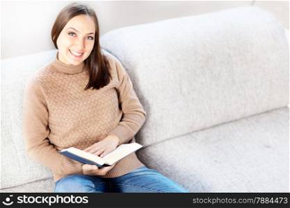 Photo of casual smiling woman sitting on the sofa with a book