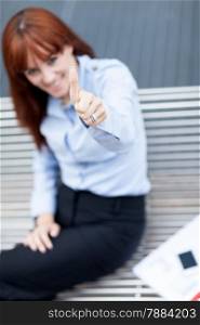 Photo of caucasian businesswoman sitting on a metal bench and making positive thumb gesture
