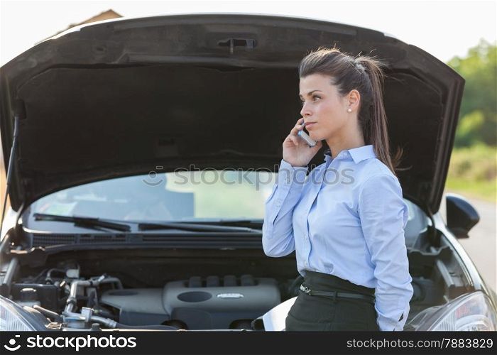 Photo of caucasian businesswoman standing next to her car and calling assistance for car problems