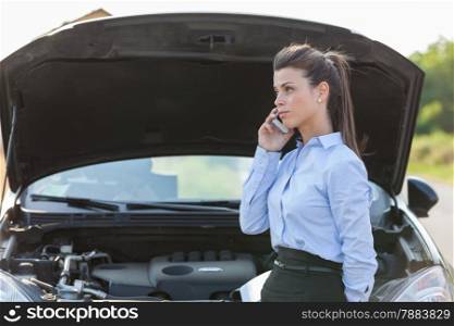 Photo of caucasian businesswoman standing next to her car and calling assistance for car problems