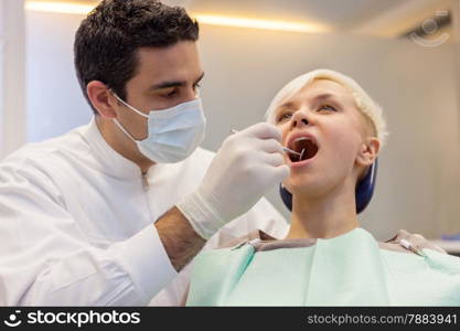photo of caucasian dentist looking inside the mouth of his young blonde patient
