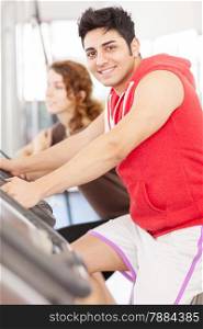 Photo of caucasian man looking at the camera while doing workout on the bicycle at the gym