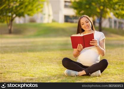 Photo of caucasian pregnant woman reading a book on a green field