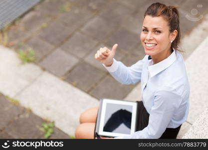 Photo of caucasian smiling businesswoman sitting outdoor and making positive thumb gesture