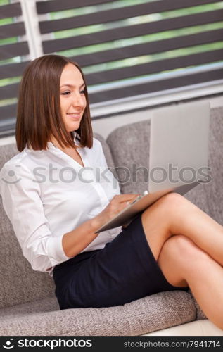 Photo of caucasian smiling businesswoman with notebook sitting on the sofa at home