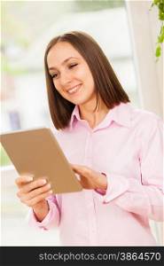 Photo of caucasian smiling woman with a pink shirt looking at her tablet pc