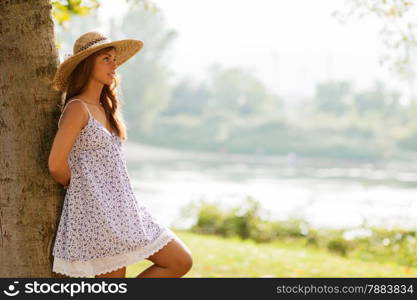 photo of caucasian smiling woman with hat behind a tree in the park