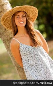 photo of caucasian smiling woman with hat behind a tree in the park