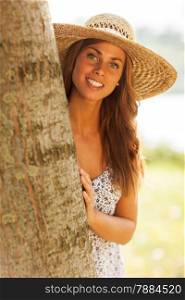 photo of caucasian smiling woman with hat behind a tree in the park