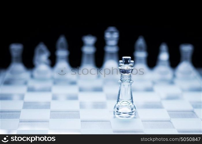 Photo of chess king standing in front of the other colour set in bright background.