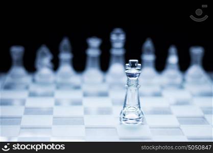 Photo of chess king standing in front of the other colour set in bright background.
