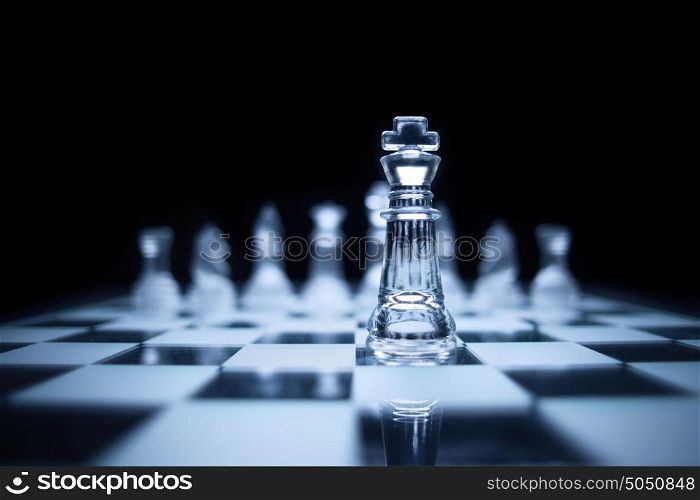 Photo of chess king standing in front of the same colour set in black background.