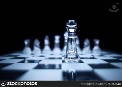 Photo of chess king standing in front of the same colour set in black background.