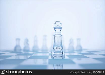 Photo of chess king standing in front of the same colour set in bright background.