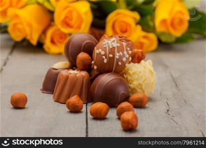 Photo of chocolate pralines and yellow roses over wooden table