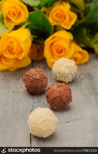 Photo of chocolate pralines and yellow roses over wooden table