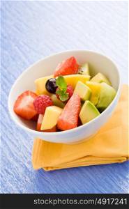 photo of colorful fruit salad on blue glass table with small mint leaf